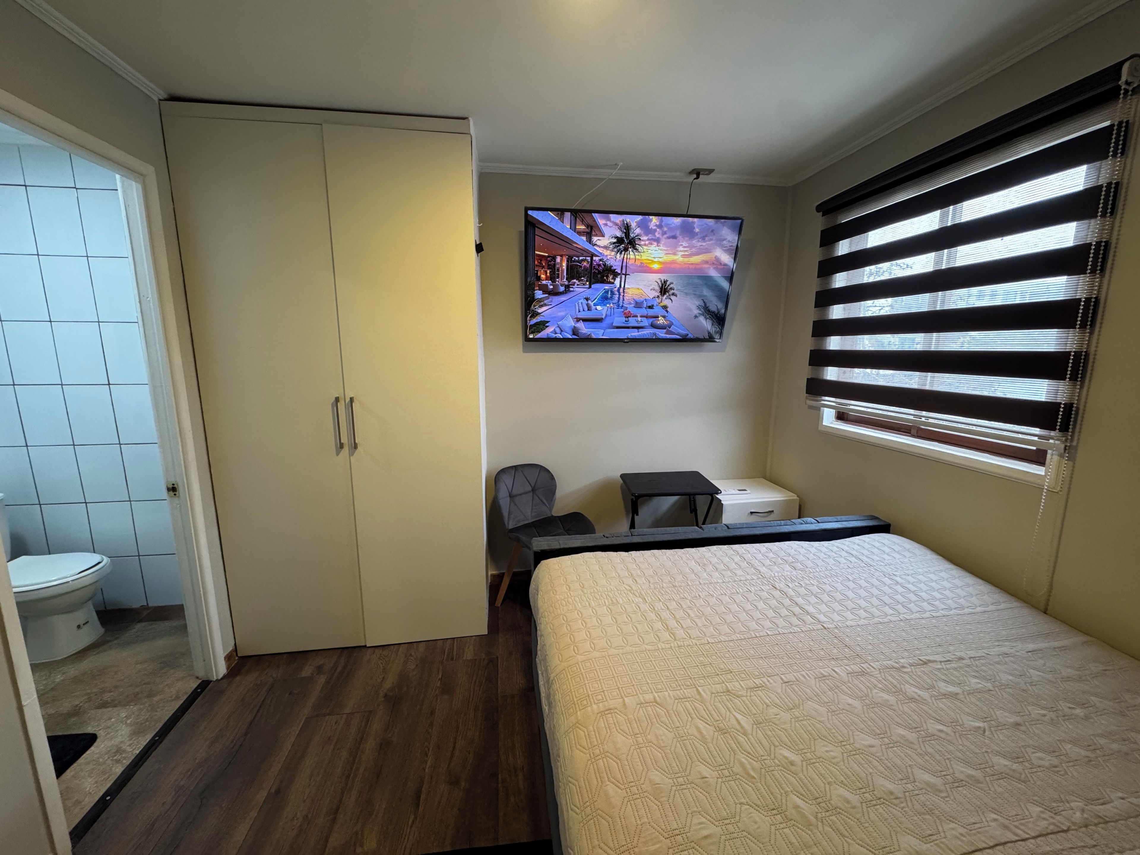 Een slaapkamer met een bed, een wandtelevisie, een bureau en een stoel.