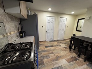 A compact kitchen with a gas stove, a refrigerator, and a dining table with chairs.