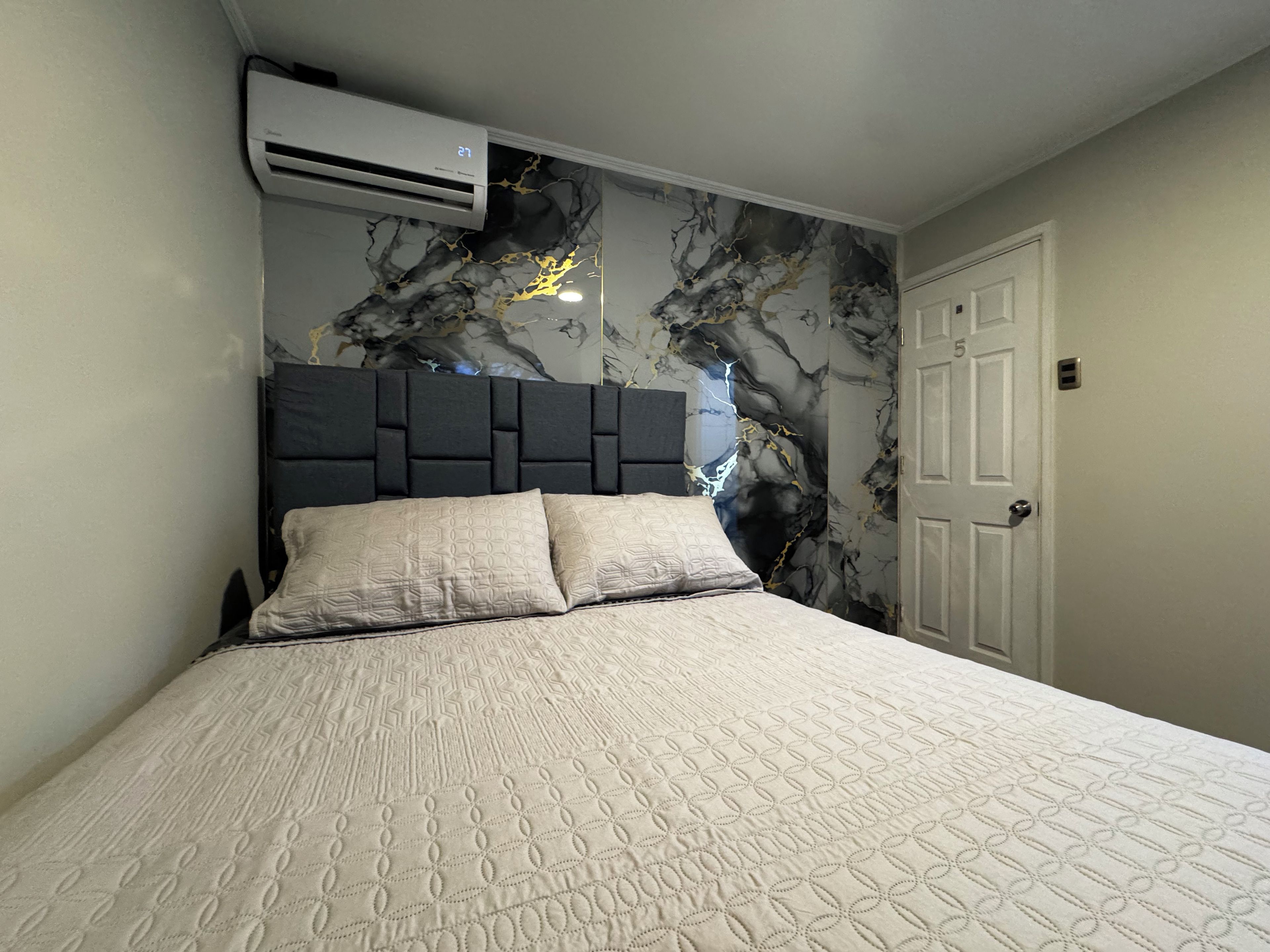 A bedroom with a bed, a headboard, an air conditioning unit, and a door.