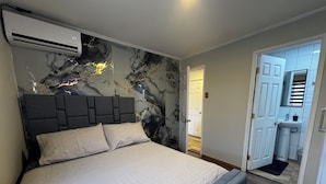 Une chambre à coucher avec un lit, une tête de lit et un mur orné d’un motif rappelant le marbre.