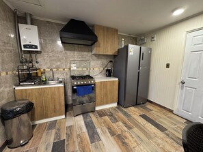 A kitchen with a gas stove, stainless steel appliances, a black range hood, and a tiled backsplash. - Tranquil studio with AC in beautiful Talca city center (Talca)