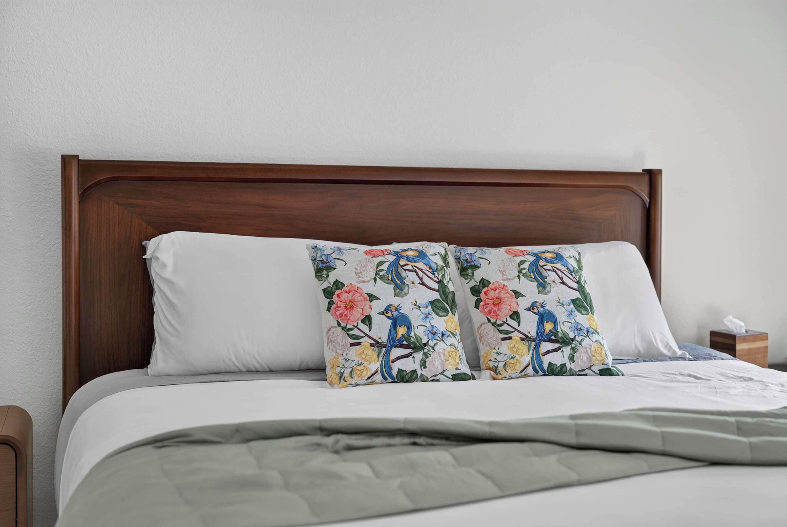 A bed with a wooden headboard, white pillows, and a floral-patterned pillow.