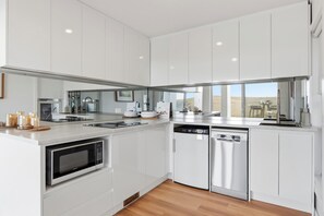 A modern kitchen with white cabinetry, stainless steel appliances, and a view of the desert landscape. - Absolute oceanfront is a cosy 1 bedroom studio overlooking the ocean. (Kiama Heights)