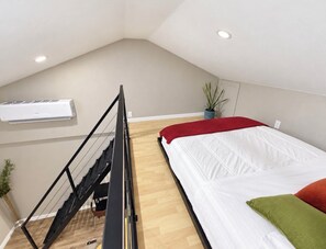 Een slaapkamer met een bed, een trap, een airconditioning en een potplant.