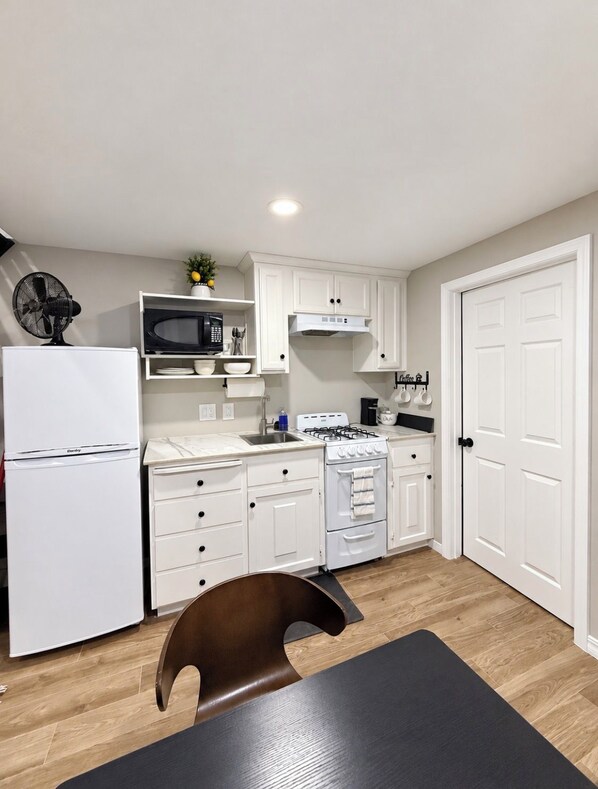 A compact kitchen with white cabinetry, a gas stove, a microwave, and a refrigerator.