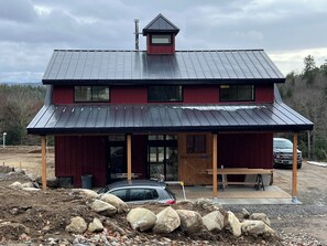 A two-story building with a metal roof, a covered porch, and a car parked in front.