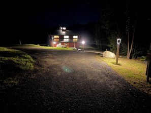 A building with a metal roof and multiple windows, surrounded by a gravel driveway and a grassy area.