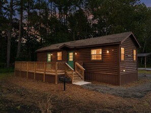 A wooden cabin with a deck, a green door, and a small porch.