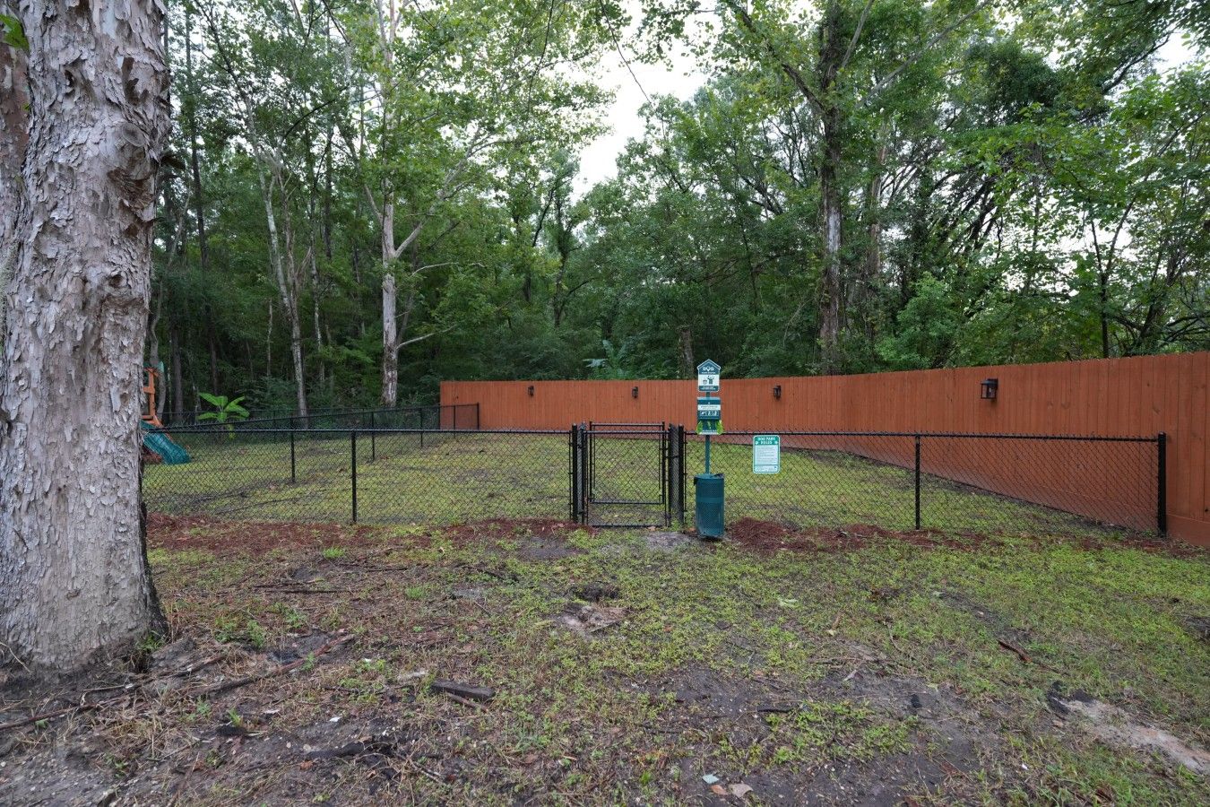 A fenced outdoor area with a wooden fence, a signpost, and a tree.