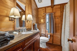 Ein Badezimmer im Holzblockhaus-Stil mit Waschbecken, Spiegel, Handtuchhalter und Toilette.