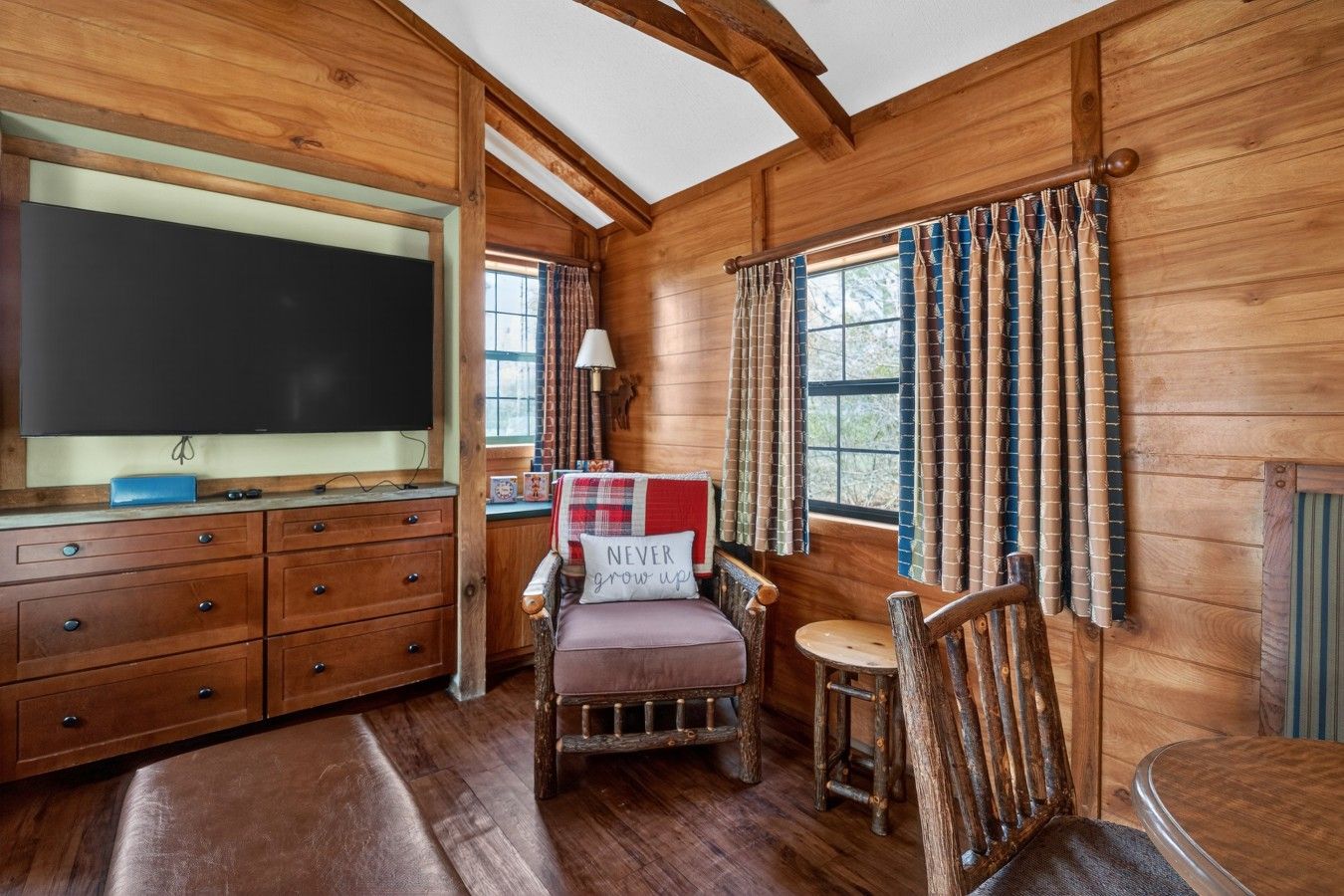 A cozy cabin interior with wooden walls, a large flat-screen TV, a wooden bench, and a small table.