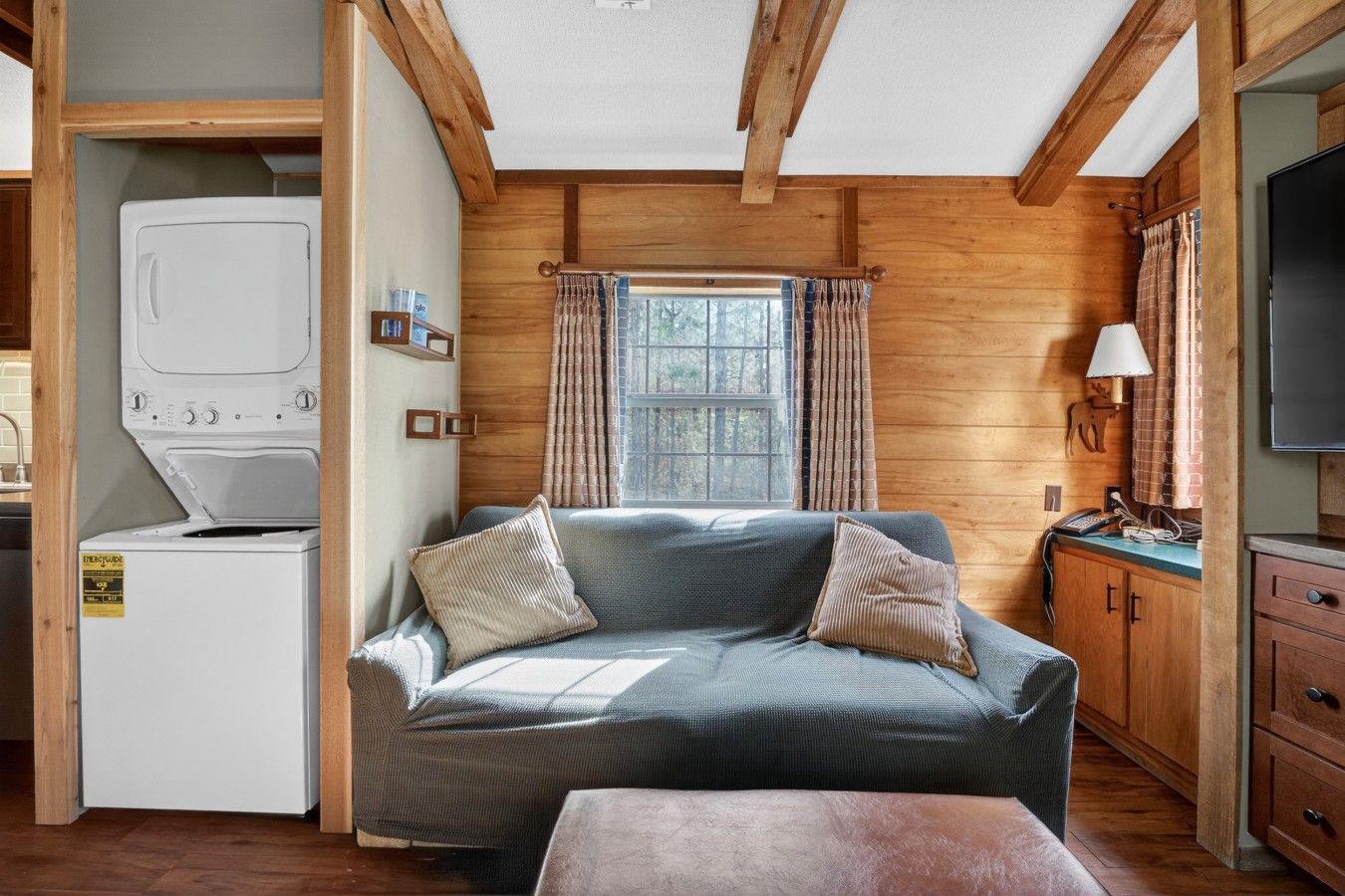A compact room with a sofa, a washing machine, a television, and a window with curtains.