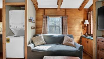 A compact room with a sofa, a washing machine, a television, and a window with curtains.
