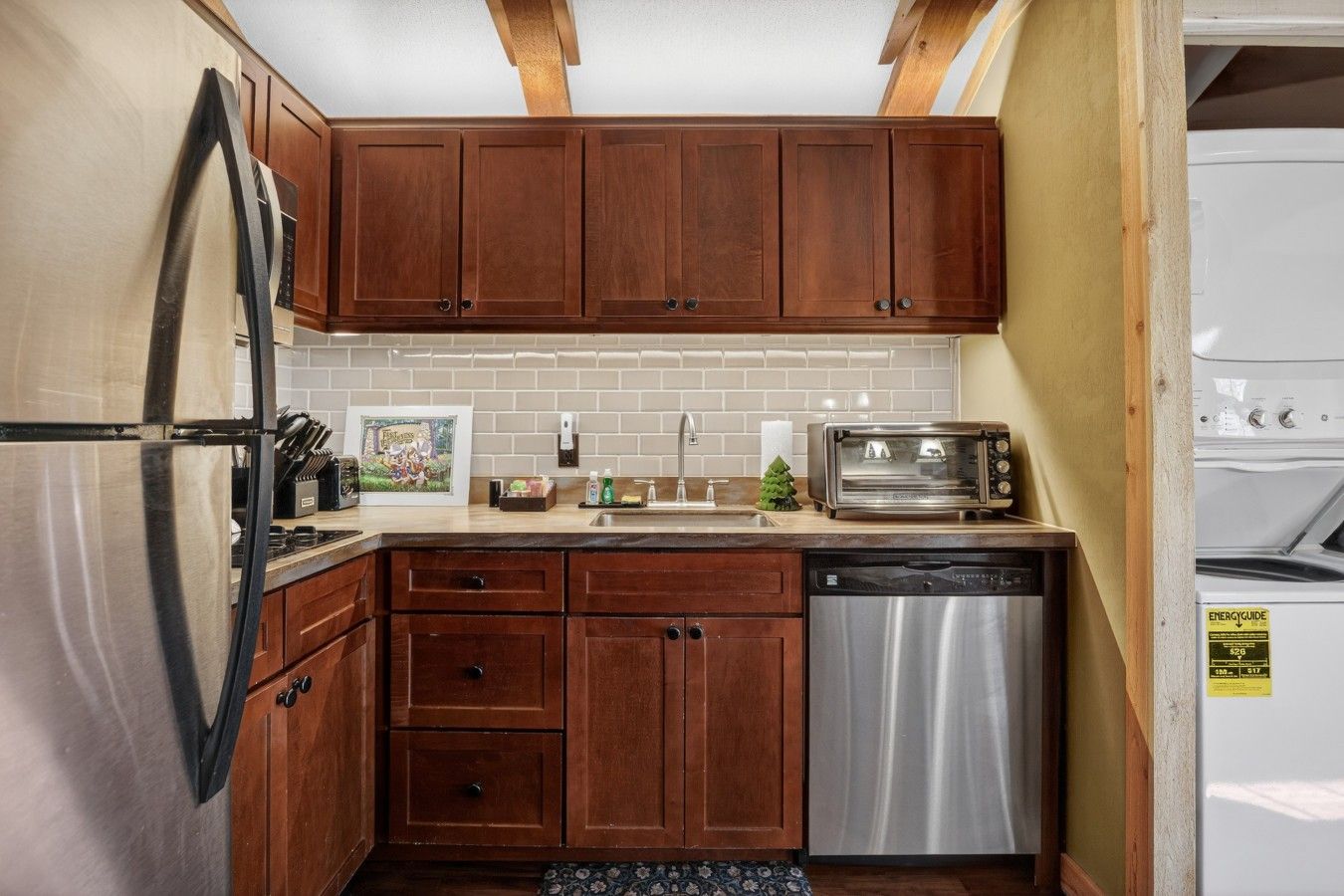 A compact kitchen with wooden cabinets, a stainless steel refrigerator, a dishwasher, and a toaster.