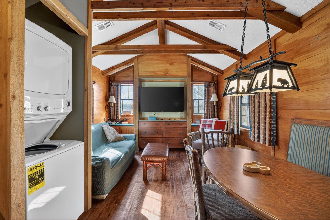 A cozy cabin interior with a dining table, sofa, and a large flat-screen TV.