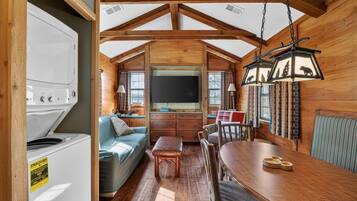 A cozy cabin interior with a dining table, sofa, and a large flat-screen TV.