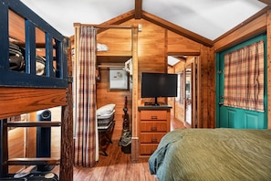 A compact, wooden cabin-style room with a bed, a television, a small desk, and a window with curtains.