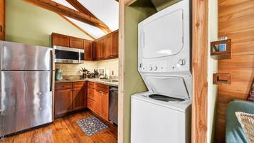 A compact kitchen with wooden cabinets, a stainless steel refrigerator, a microwave, and a washing machine.