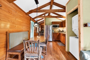 A wooden interior with a dining table, chairs, a bench, a refrigerator, a microwave, and a washing machine.