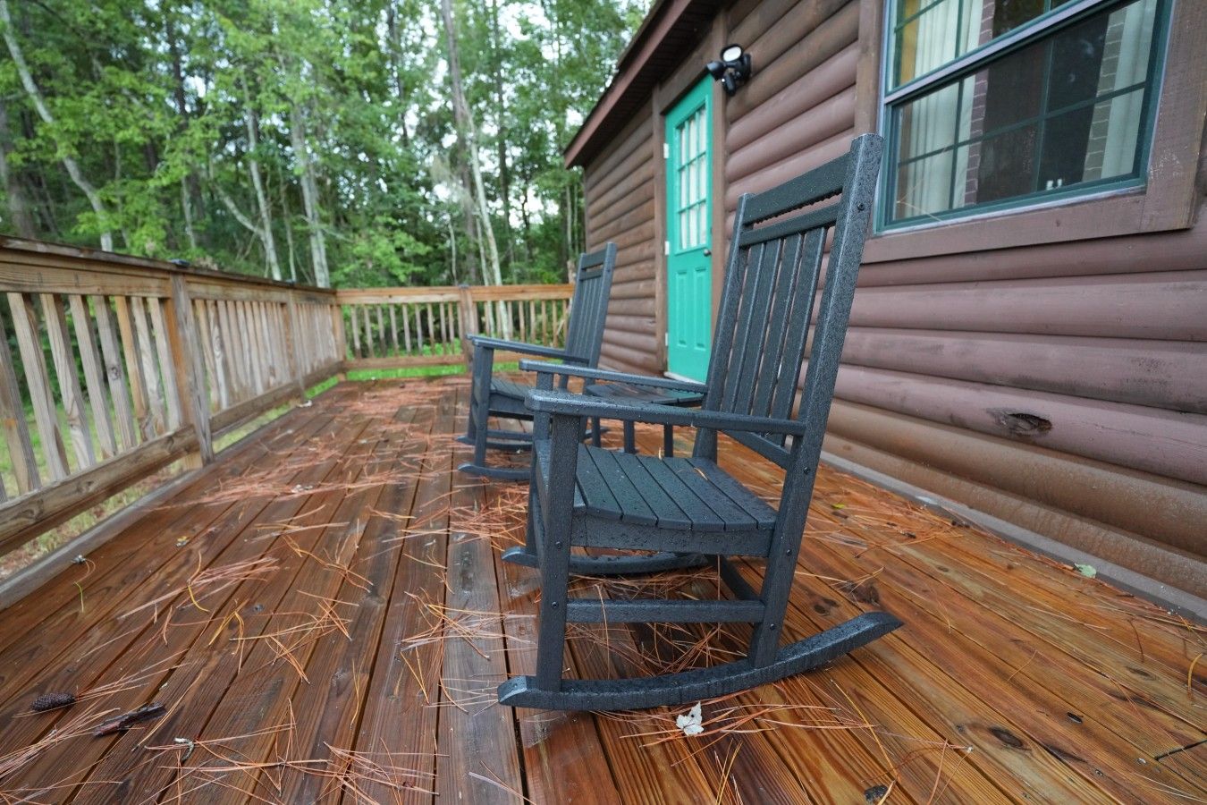 A wooden deck with two rocking chairs and a cabin with a green door.