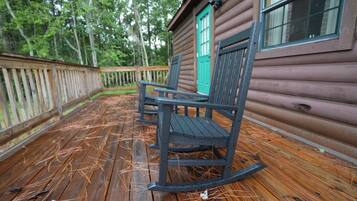A wooden deck with two rocking chairs and a cabin with a green door.