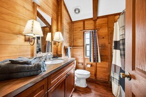 A wooden interior with a bathroom that includes a sink, two wall-mounted lamps, a toilet, and a shower curtain.