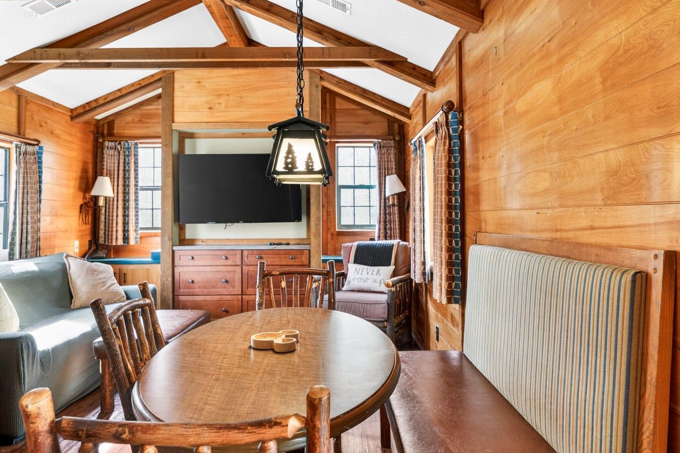 Ein gemütliches Blockhaus-Interieur mit einem Holztisch, Stühlen, einer Couch und einem Fernseher.