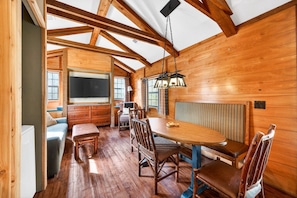 A wooden interior with a dining area, a television, and a window. - Sycamore Cabin · Fenced Dog Park + Playground (Callahan)