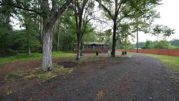 A gravel driveway leading to a wooden cabin with a fenced yard and trees.