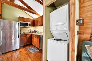 A compact kitchen with wooden cabinets, a stainless steel refrigerator, a microwave, and a washing machine. - Sycamore Cabin · Fenced Dog Park + Playground (Callahan)
