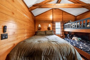 A cozy wooden cabin bedroom with a bunk bed, two bedside lamps, and a window. - Sycamore Cabin · Fenced Dog Park + Playground (Callahan)