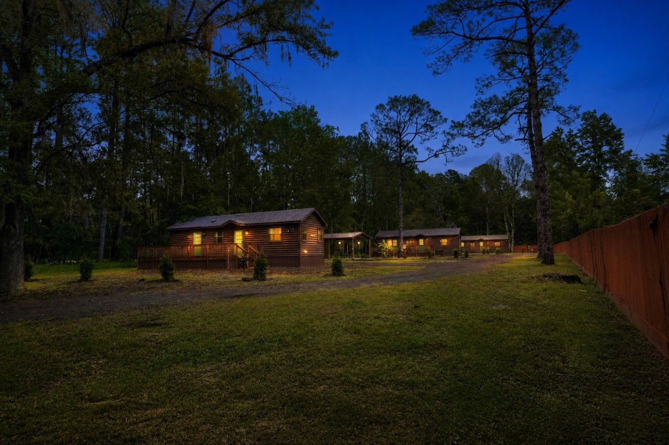 A row of cabins with a wooden deck and a covered area, surrounded by trees.