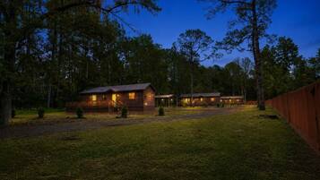 A row of cabins with a wooden deck and a covered area, surrounded by trees.