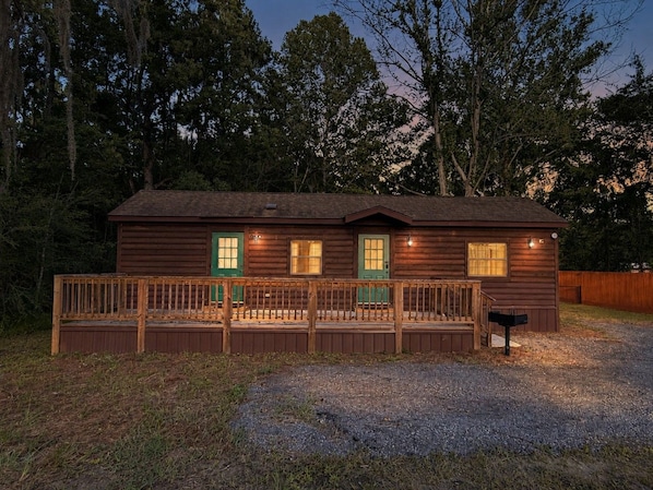 A wooden cabin with a porch, a mailbox, and a gravel driveway.