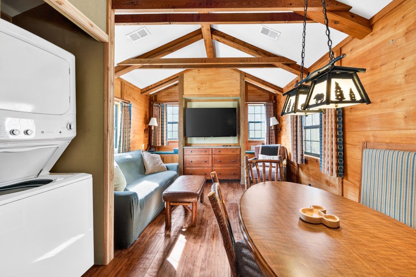 L'intérieur d'un chalet chaleureux, avec une table à manger en bois, un canapé et un téléviseur.