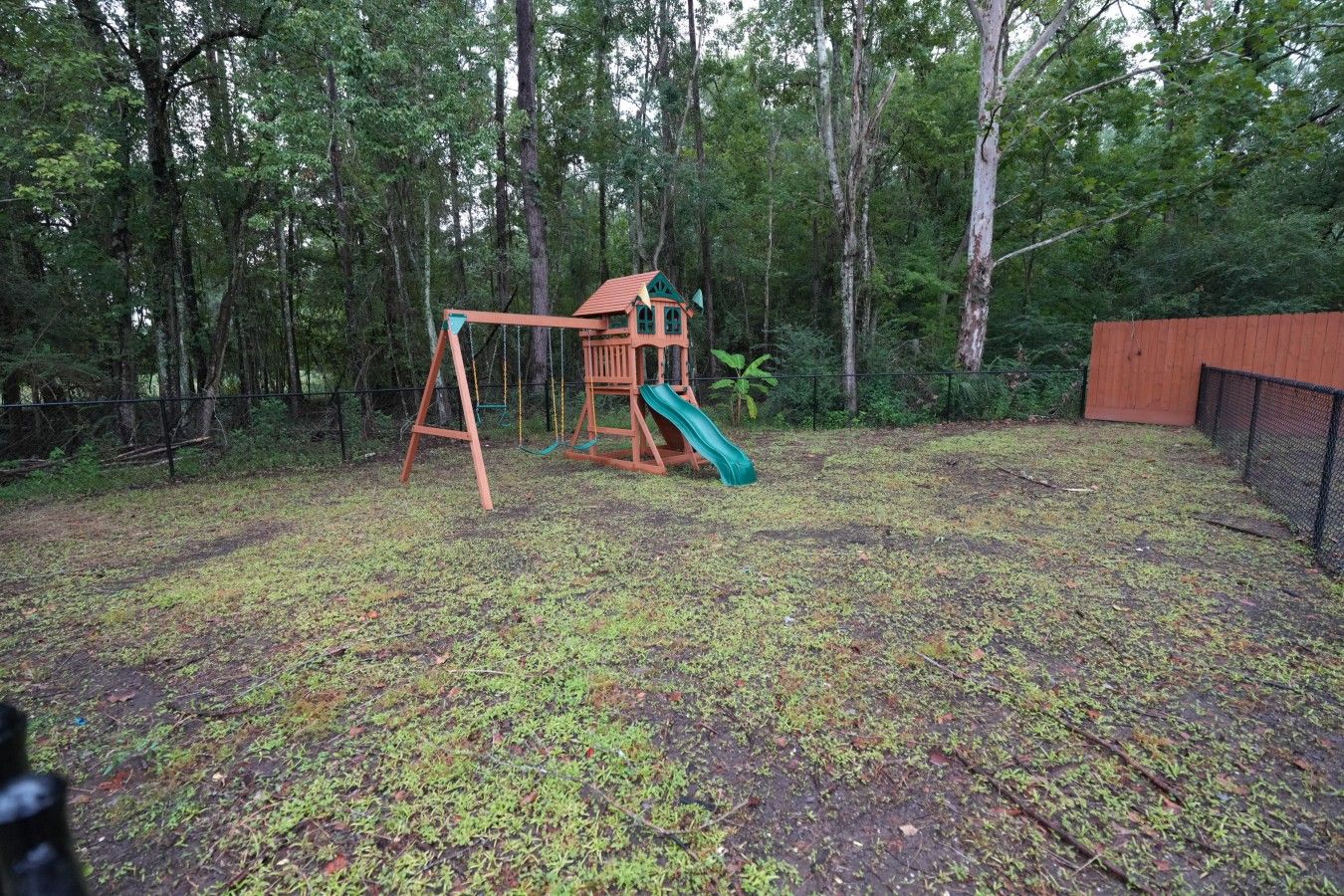 A wooden swing set with a slide in a wooded backyard.