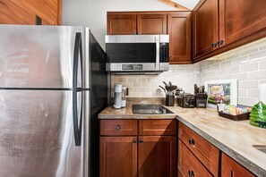 A kitchen with a stainless steel refrigerator, a microwave, wooden cabinets, a countertop with a coffee maker, and a knife block.