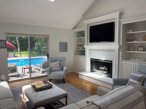 A living room with a fireplace, a television, and a pool view. - 4-bedroom house in Westhampton Beach 1 mile to Main Street. Pool and Hot Tub (Westhampton Beach)