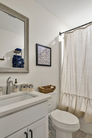 Un baño con un lavamanos blanco, inodoro, espejo enmarco y cortina de ducha.