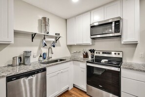 A modern kitchen with white cabinets, a stainless steel dishwasher, a built-in oven, and a microwave. - 8 Min to Duke + DT | Free Parking + Wi-Fi (Durham)