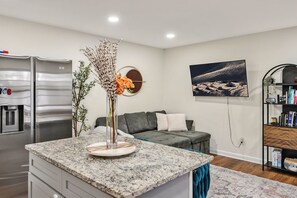 A modern kitchen with a granite countertop, a built-in refrigerator, and a dining area with a grey sofa. - 8 Min to Duke + DT | Free Parking + Wi-Fi (Durham)