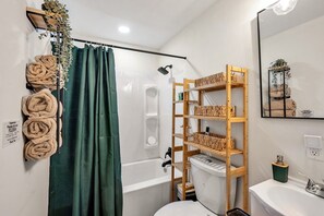 A bathroom with a shower, toilet, and a shelf with towels. - 8 Min to Duke + DT | Free Parking + Wi-Fi (Durham)