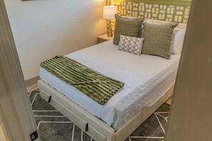 Un letto rifatto con una coperta verde, una lampada da comodino e cuscini decorati.