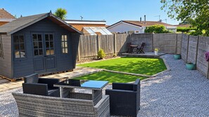 Ein Garten mit Terrasse, einer kleinen Gartenhütte und einem umzäunten Bereich.