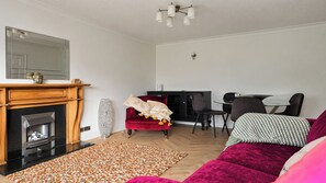 Ein Wohnzimmer mit Kamin, einem roten Sofa, einem gemusterten Teppich und einem Essbereich mit Stühlen und Tisch.