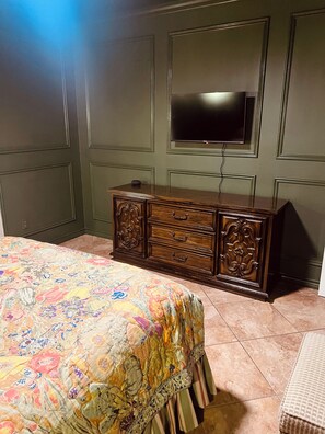 Un dormitorio con cama, cómoda, televisor y colcha estampada.