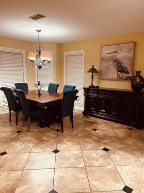 Un comedor con una mesa y sillas de madera, una araña y un cuadro en la pared.