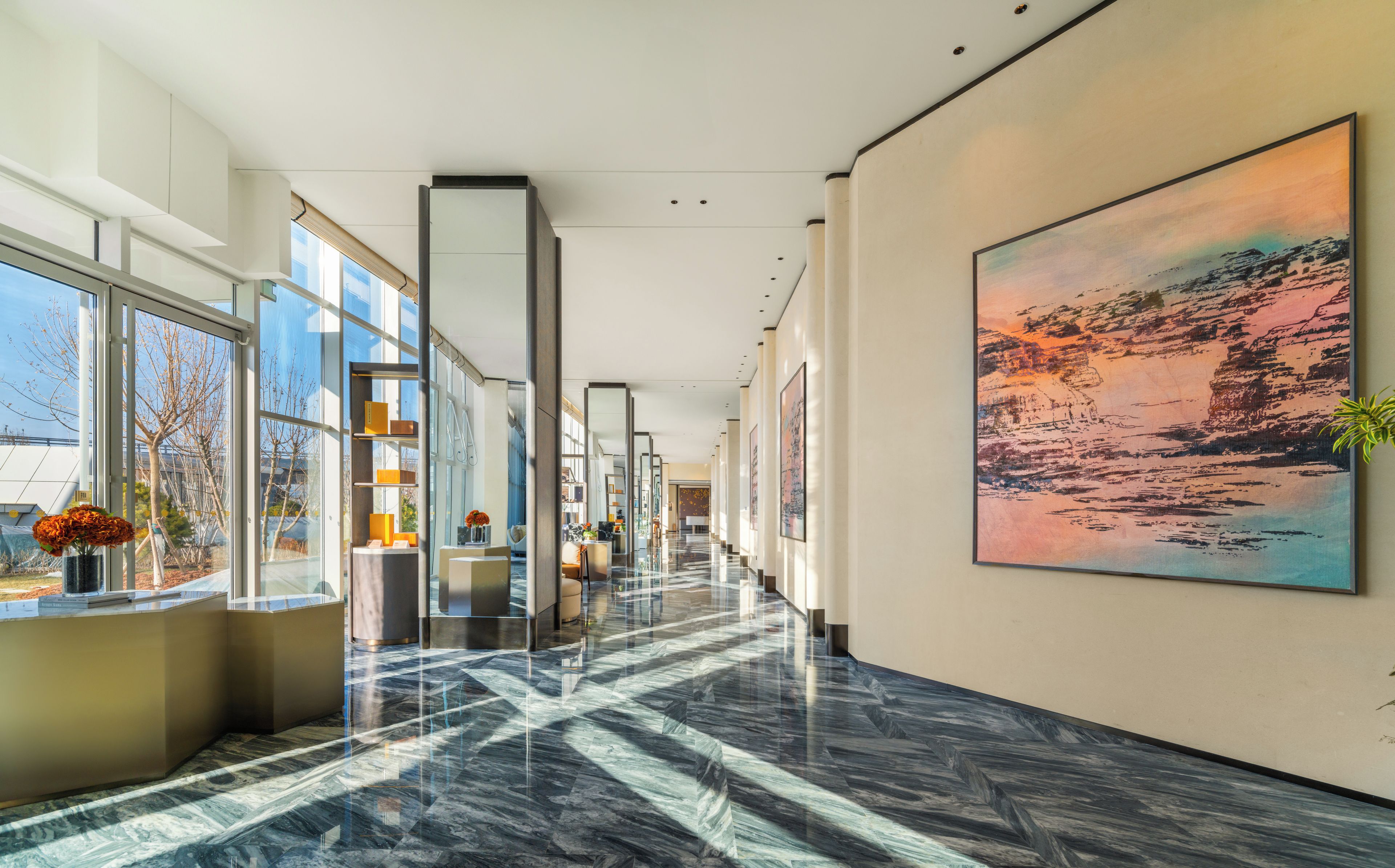 Un moderno hall de hotel con piso de mármol, amplias ventanas y obras de arte en las paredes.