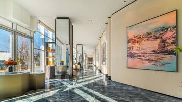 Un moderno hall de hotel con piso de mármol, amplias ventanas y obras de arte en las paredes.