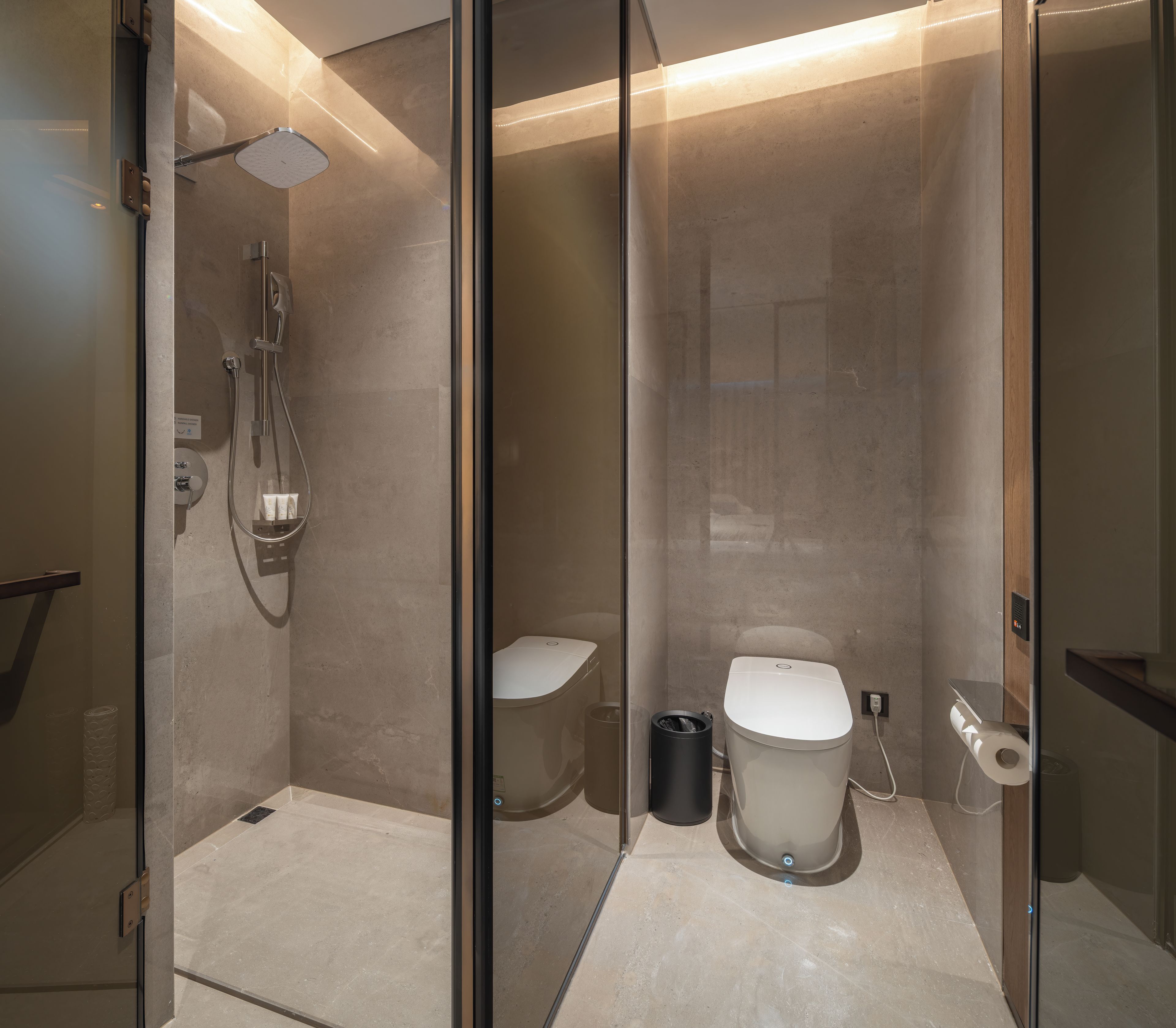 A modern bathroom with a glass partition, a shower, a toilet, and a bidet.